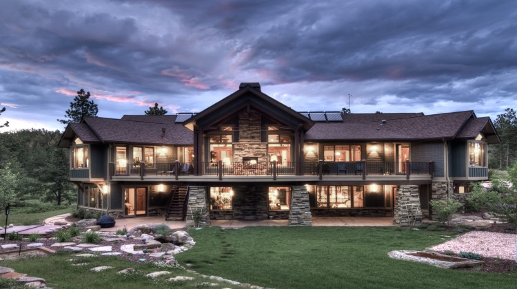 Large stone and wood house exterior photographed at dusk with lit windows, balconies, and a dramatic cloudy sky